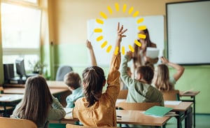 Bambini in classe con le mani alzate durante una lezione coinvolgente