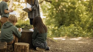 Bambini scuola primaria scrivono su taccuini intorno a un tronco di legno in un’aula didattica all’aperto