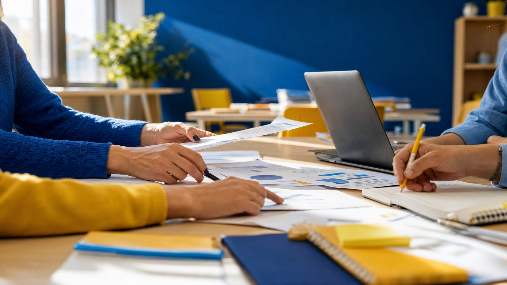 Dettaglio mani che consultano documenti stampati e appunti su tavolo studio luminoso accanto a laptop, contesto formazione docenti